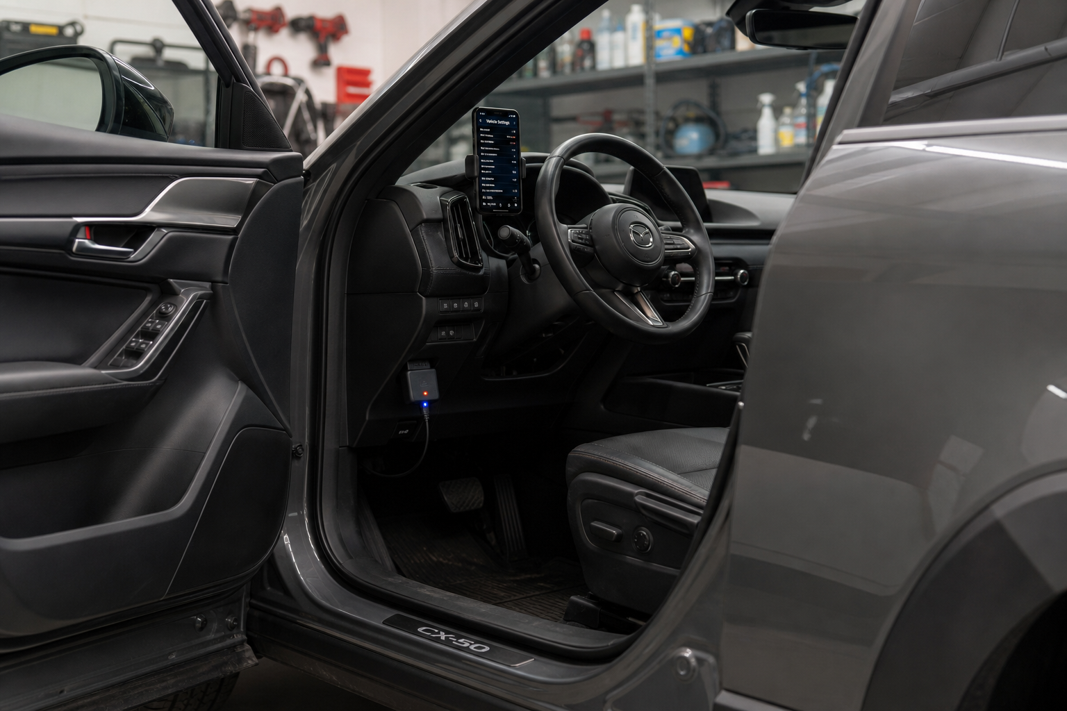 An OBD2 dongle plugged into a Mazda CX-50 with a smartphone showing vehicle settings