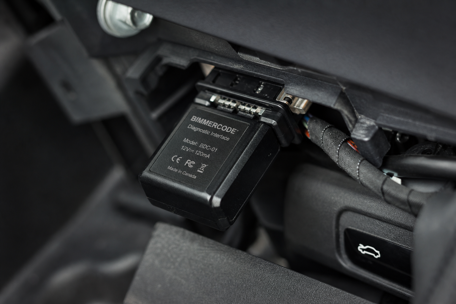 Small electronic start/stop eliminator module plugged into a BMW connector port under the dashboard