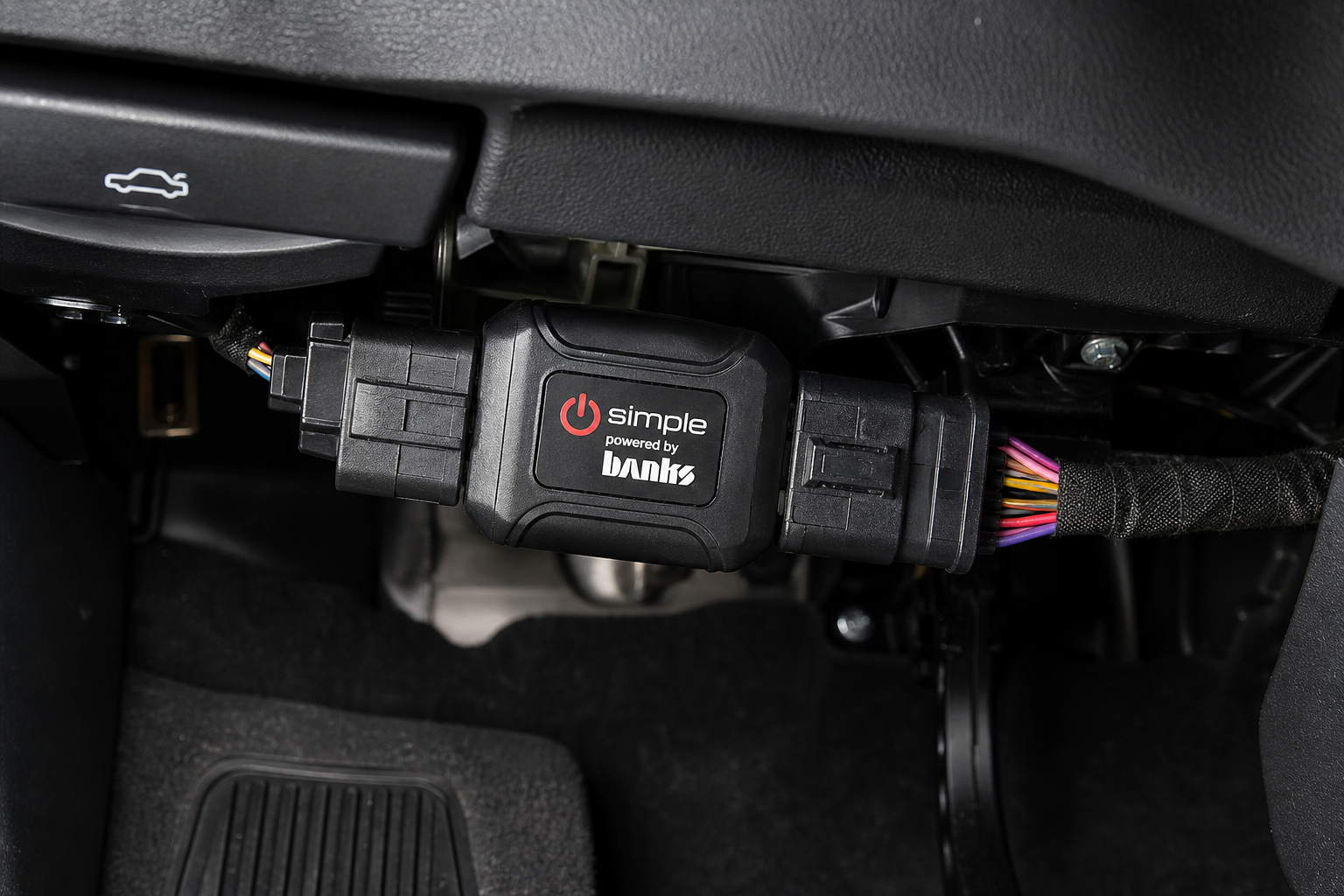 A start/stop eliminator module plugged into a vehicle wiring harness under the dashboard