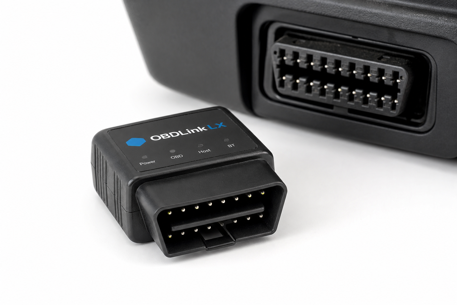 Small automotive Start/Stop eliminator module placed next to an OBD connector on a white surface