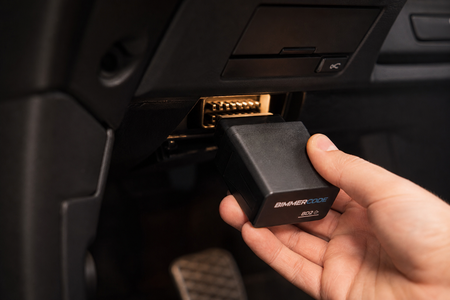 A start/stop eliminator module being plugged into the OBD2 port under a BMW dashboard