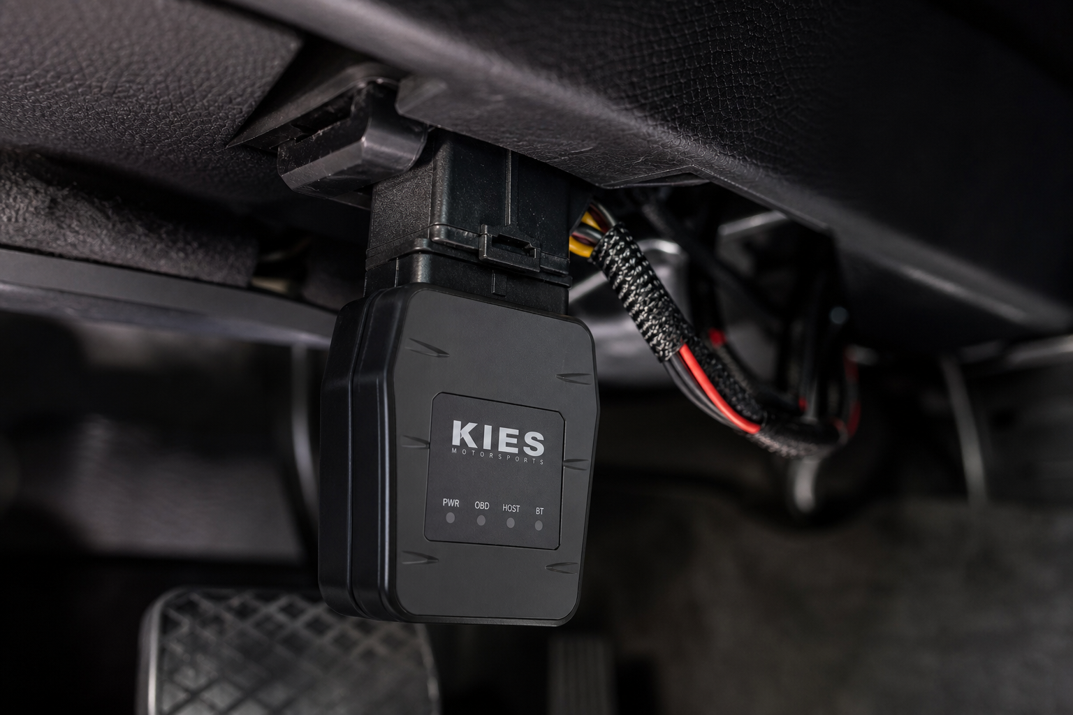 A start/stop eliminator module plugged into a vehicle wiring harness connector under the dashboard