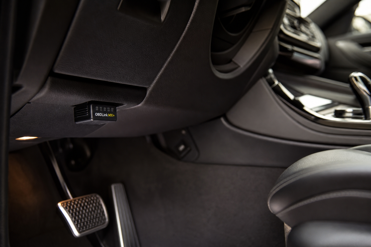 A start/stop eliminator module plugged into the OBD2 port under a BMW 3 Series dashboard