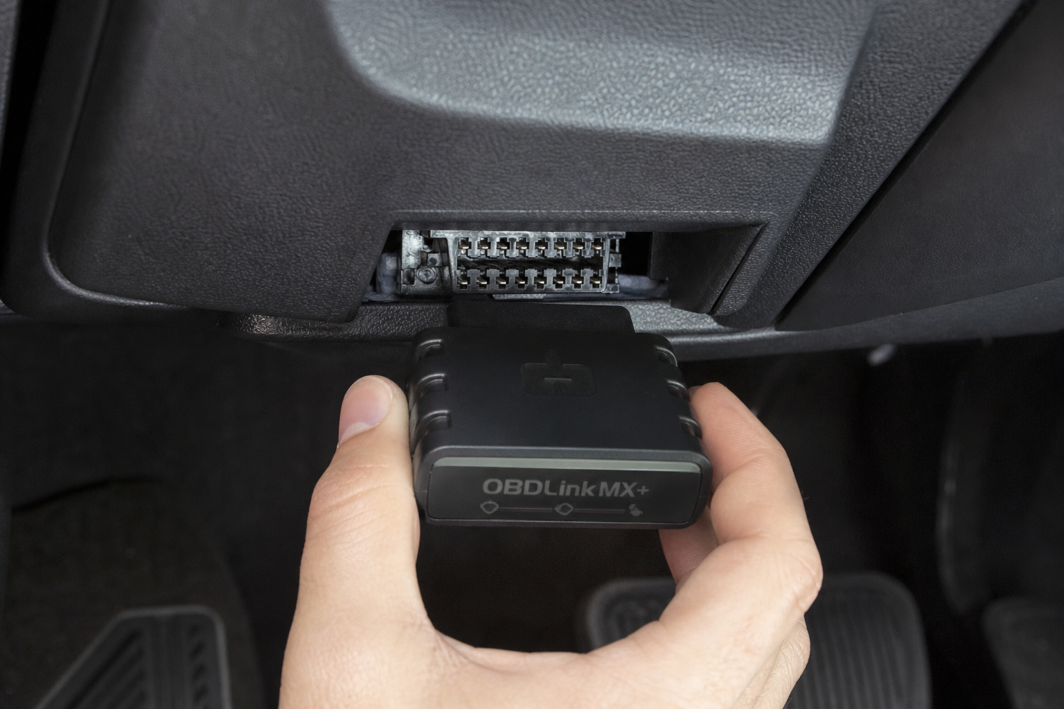 A small plug-and-play electronic module being inserted into a vehicle OBD-II port under the dashboard