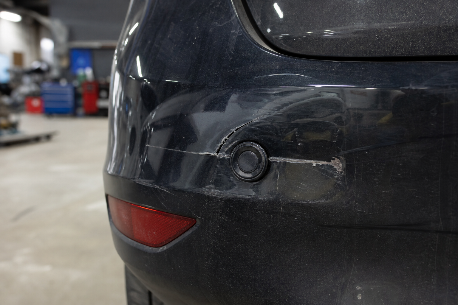 Damaged car bumper with a scrape near a parking sensor in a body shop