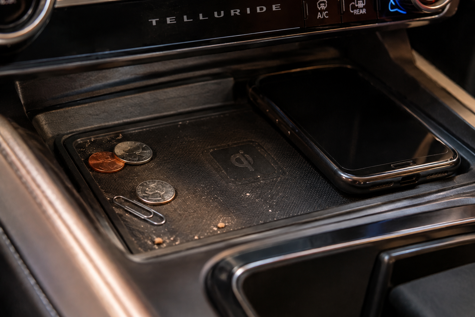 Coins and debris scattered on a car wireless charging pad next to a smartphone