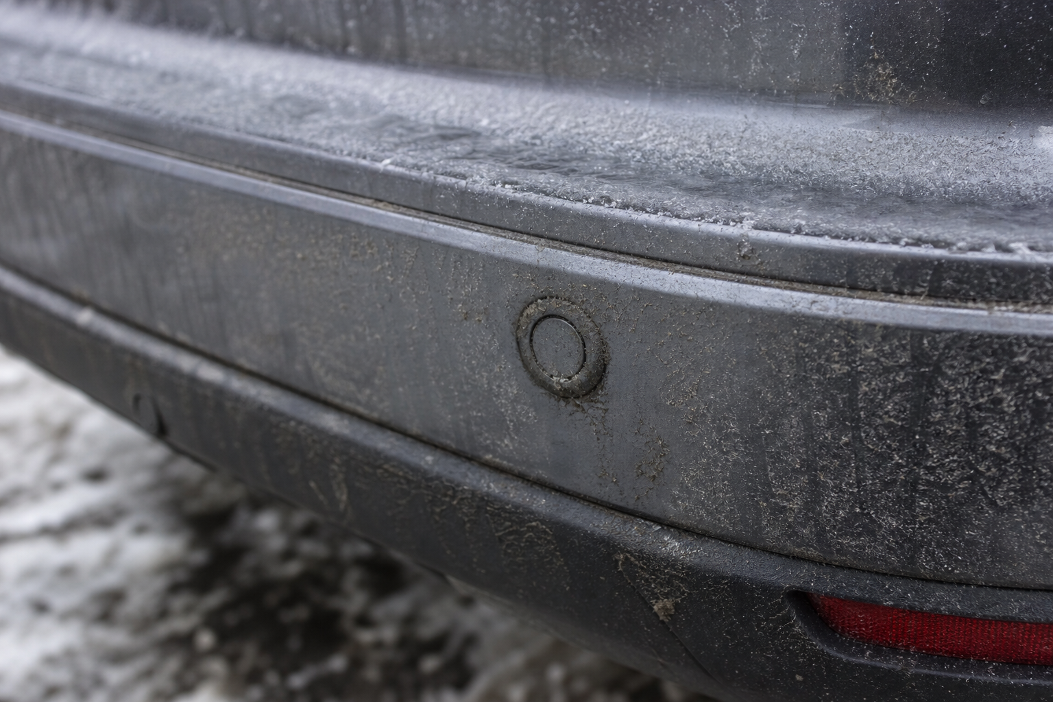 Close-up of a dirty, frost-covered parking sensor on a car bumper