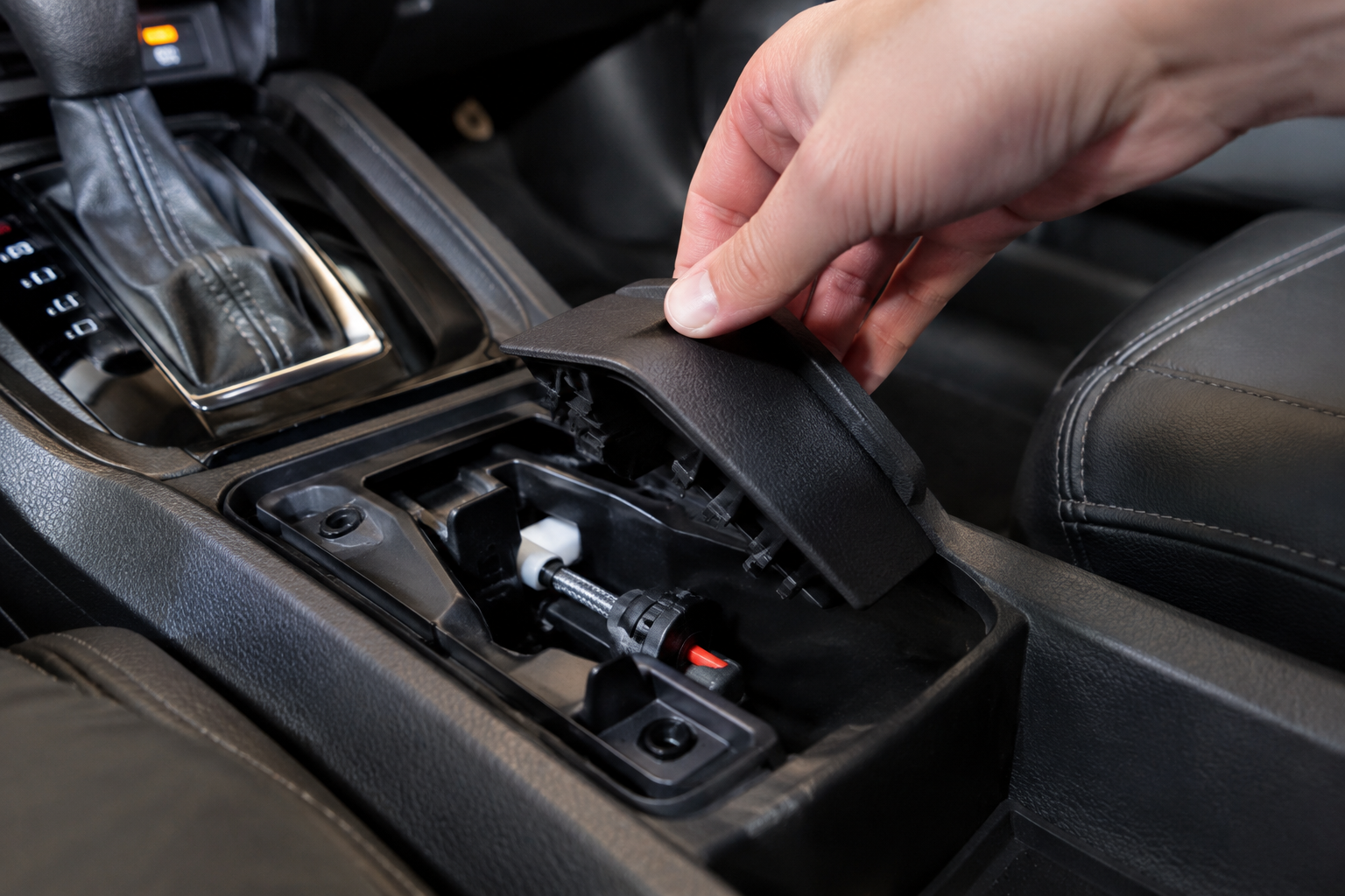 Hand accessing the manual emergency parking brake release inside a Nissan Rogue